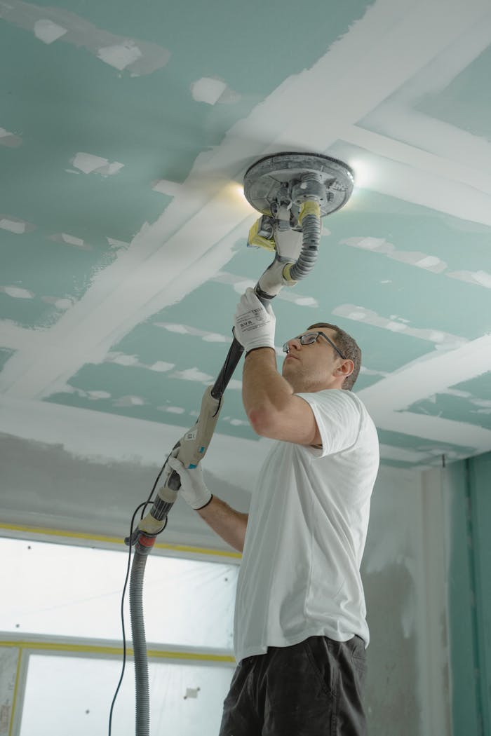 Adult male sanding a drywall ceiling with an industrial tool during home renovation.
